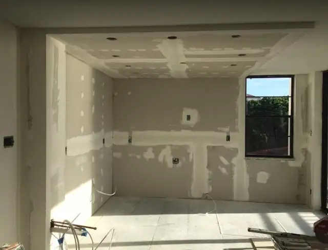 Room in the drywall and taping stage with recessed light cutouts in a dropped ceiling and a black-framed window, during a CRUSH IT Renovations remodel